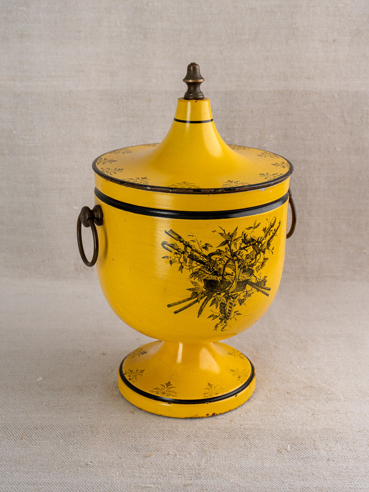 Vintage French yellow Directoire tôle peinte champagne cooler with black floral motifs, metal handles, on neutral fabric background.