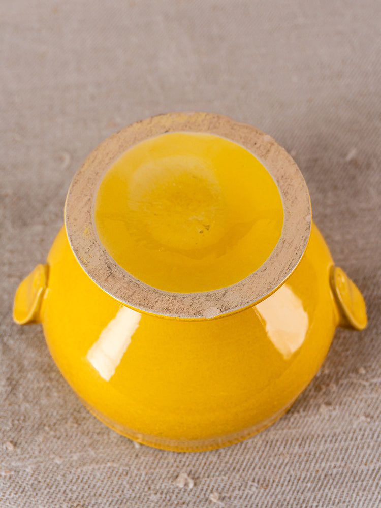 Signed Eyguières French yellow soupière, displayed upside down with side handles on gray textured surface.