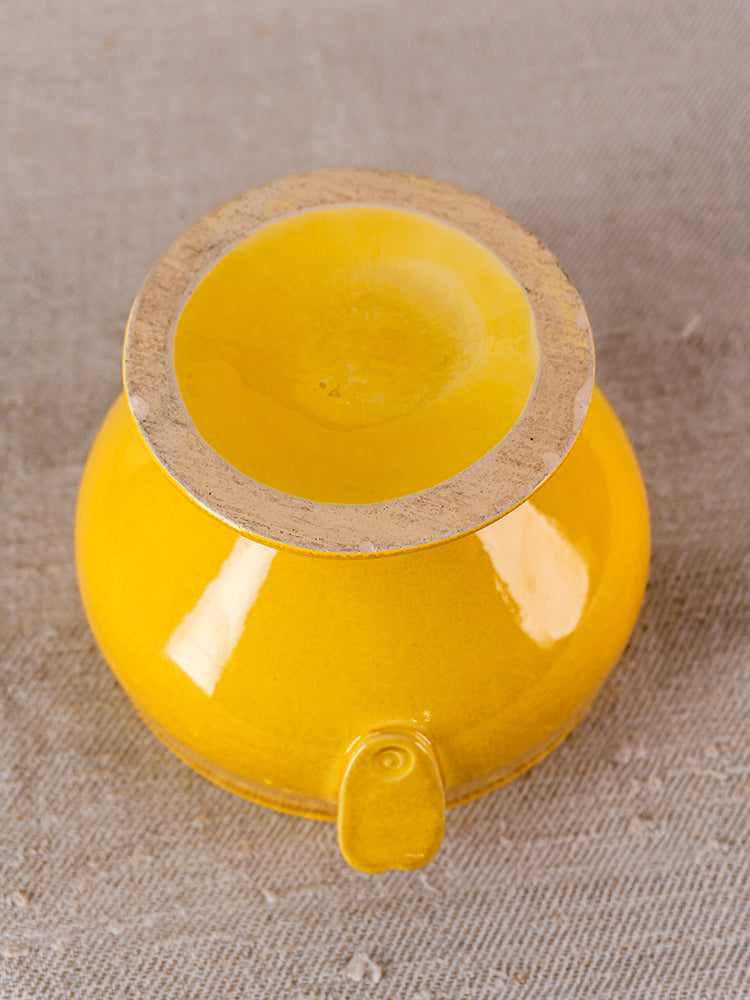 Vintage French yellow soupière tureen upside down, unglazed rim and base visible on beige textured surface.
