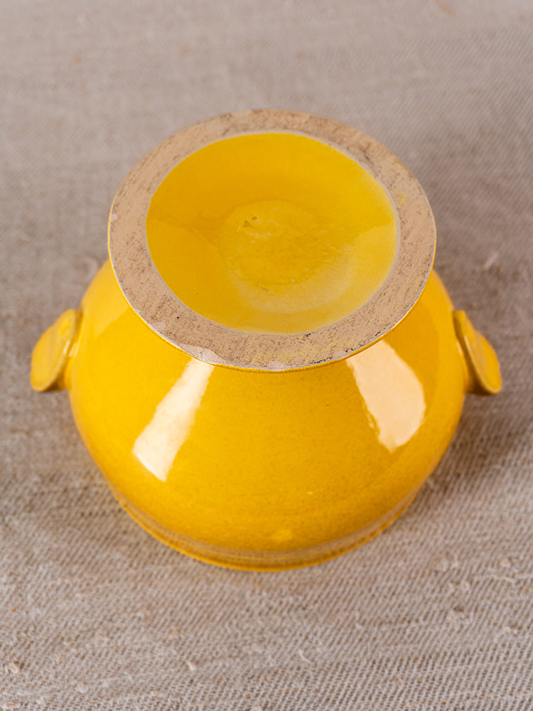 Small vintage French yellow glazed tureen with two side handles, shown upside down on beige cloth.