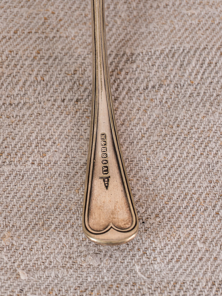 Close-up of silverware handle with hallmark stamps on beige textured fabric, reflecting Provençal elegance.