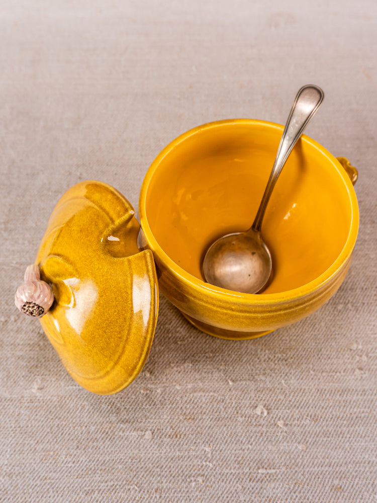 Vintage French yellow Eyguières Provençal tureen with matching lid and spoon on beige surface.