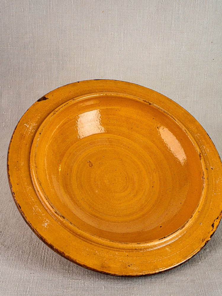Round shallow glazed terracotta bowl with slip decoration, warm amber glaze, on light gray fabric.