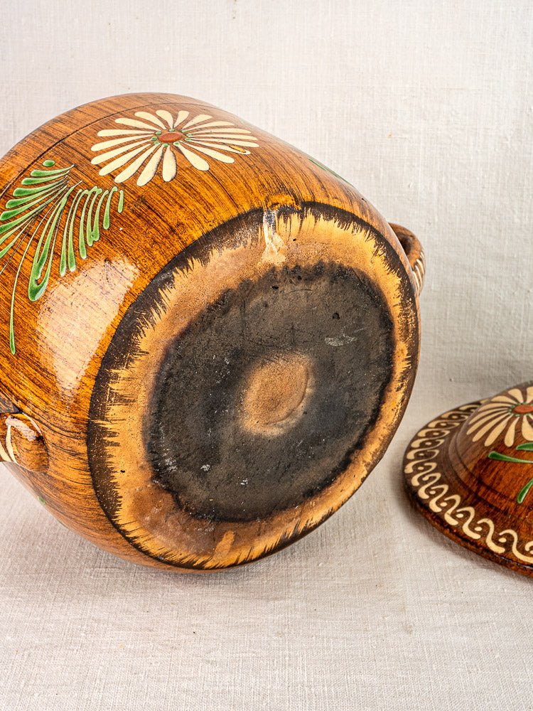 Alsace glazed terracotta cookware piece upside down, showing blackened base, beside matching lid on light fabric.
