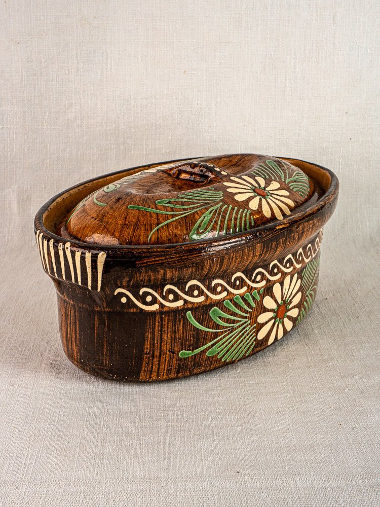 Oval slip-decorated Alsace glazed ceramic container with lid, hand-painted floral motifs, on neutral fabric.