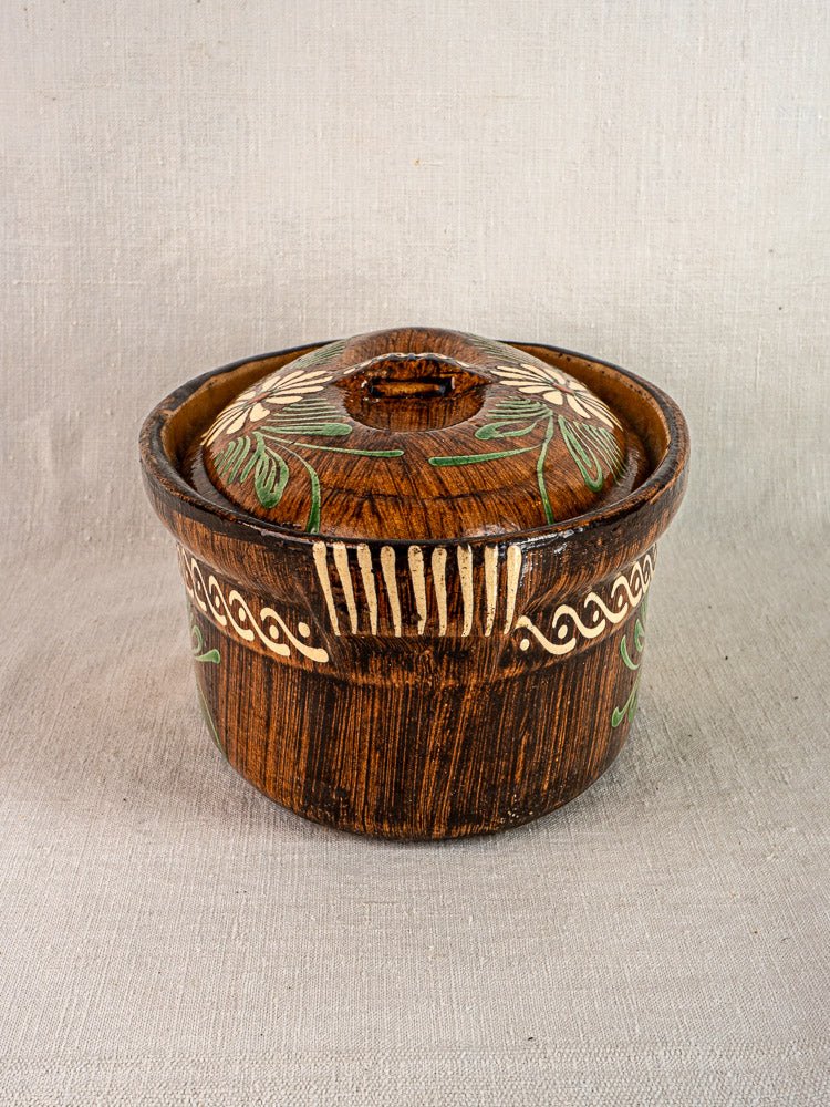 Antique French terracotta cookware set from Alsace with green, white, and beige floral motifs on neutral fabric background.