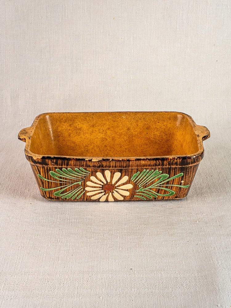 Alsace glazed terracotta baking dish with handles, floral brown exterior, yellow interior on neutral fabric.