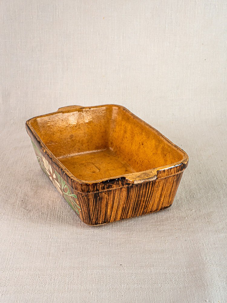 Alsace glazed terracotta baking dish with wood grain texture and hand-painted floral motifs on neutral fabric.