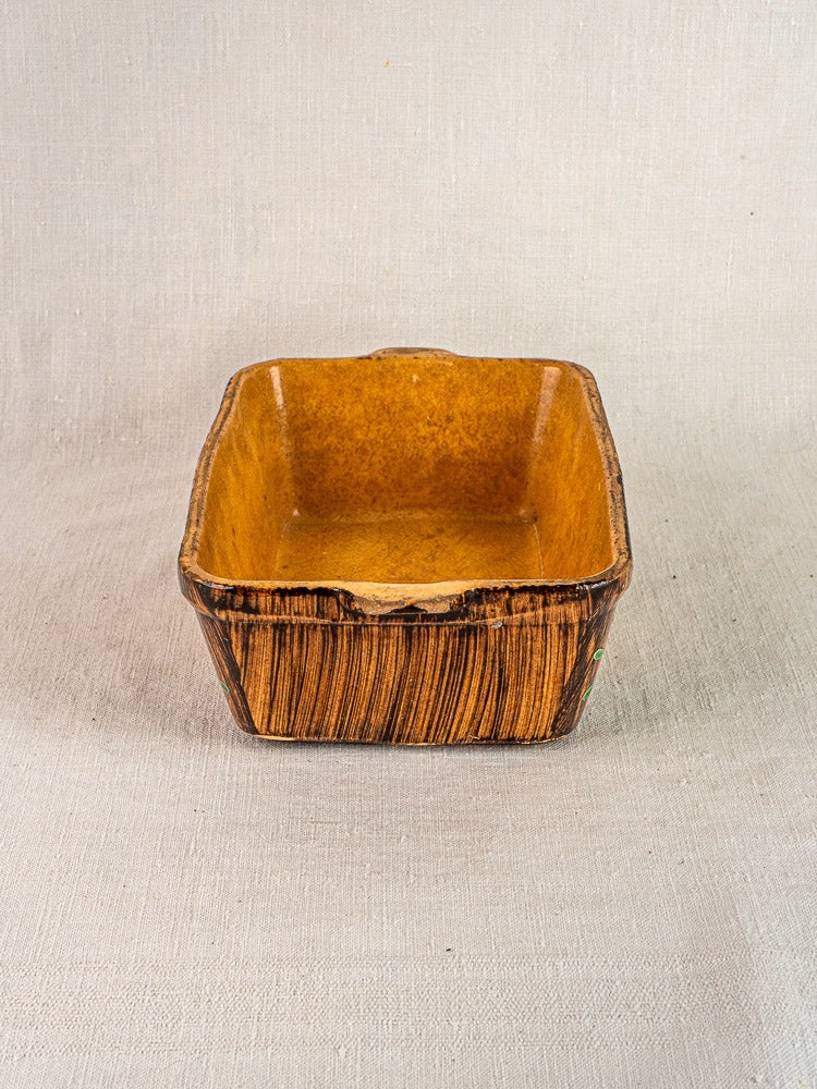 Alsace terracotta baking dish with slip decoration, yellow-brown glaze, chip on rim, on fabric.