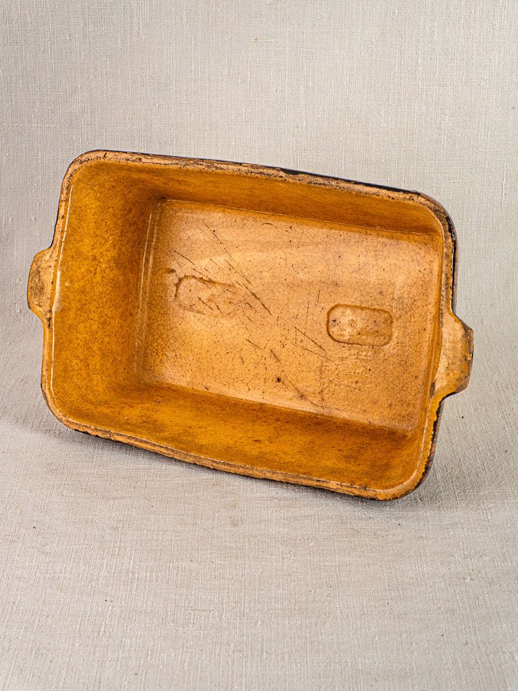 Rectangular tan Alsace terracotta dish with side handles, slip decoration, and worn earthenware interior.