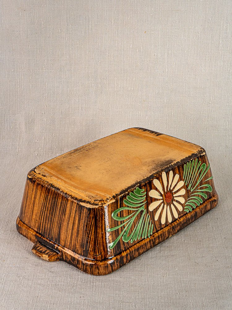 Alsace glazed terracotta rectangular dish with brown glaze and daisy slip décor on light textured surface.