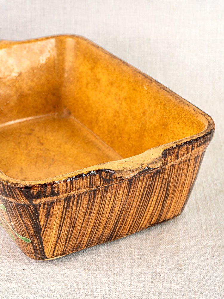 Rectangular Alsace glazed terracotta baking dish with wood-like texture, chip on rim, on light fabric.