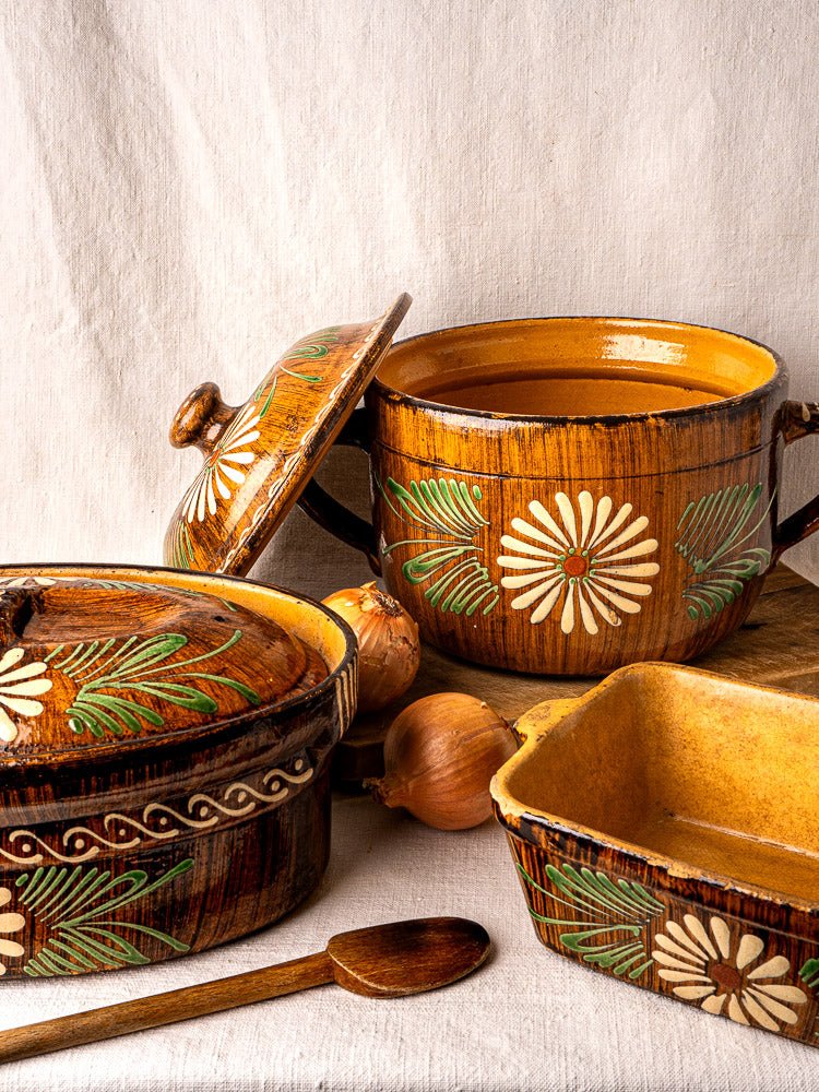Alsace glazed terracotta cookware with yellow and brown floral slip decoration, set on beige cloth with onions.