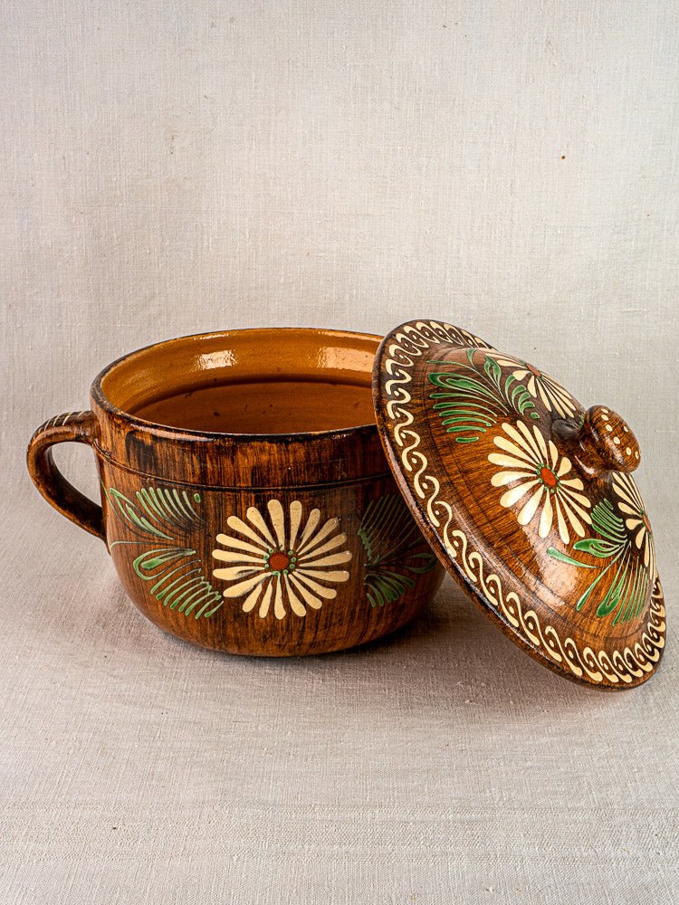 Antique French glazed terracotta cookware set with hand-painted green leaves and white flowers on earthenware, shown on light fabric.