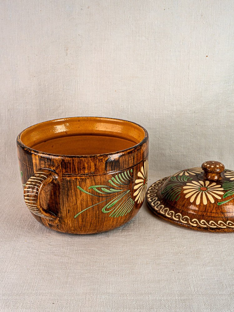 Antique French terracotta cookware set with floral slip decoration and matching lid on beige surface.
