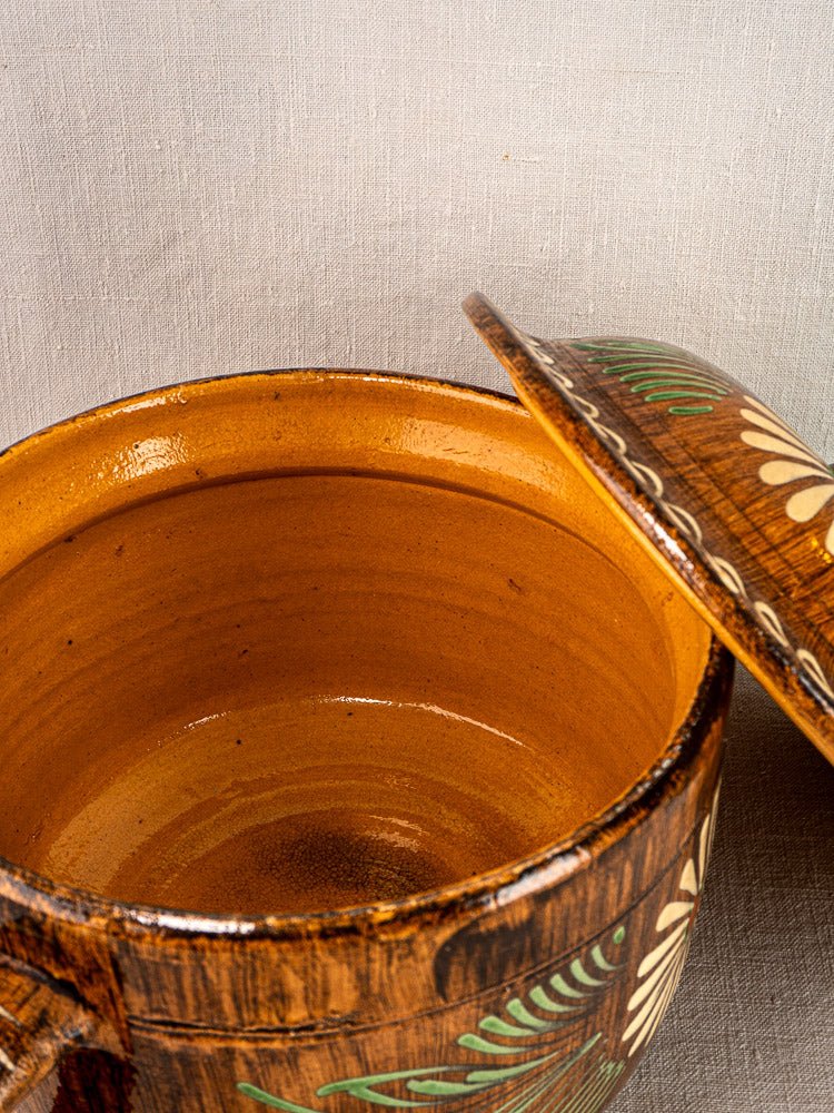 Alsace glazed terracotta cookware with slip-decorated floral motifs, partially open on beige textured surface.