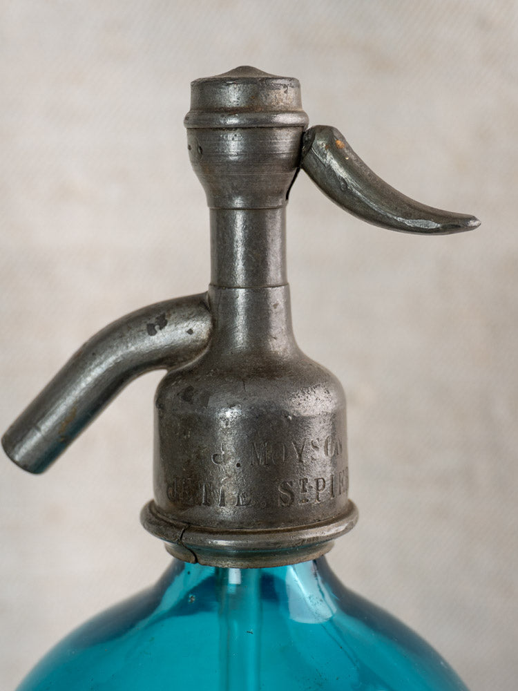 Antique Belgian soda siphon with turquoise blue glass and “Bruxelles” etched metal top, neutral background.