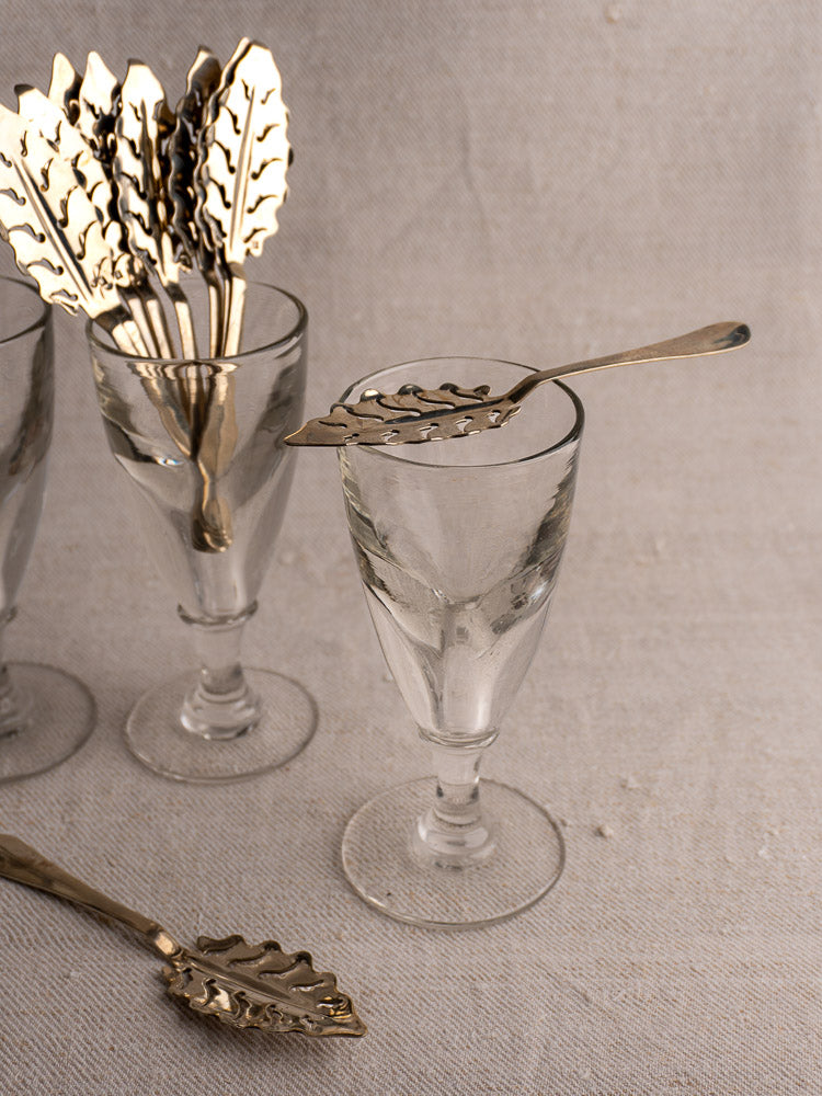 Set of 10 Antique French Absinthe Spoons by Cailar Bayard, Leaf Pattern, shown with clear glasses on fabric background.