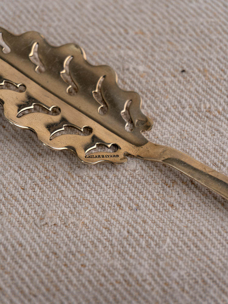 Leaf-patterned Cailar Bayard absinthe spoon with engraved name, displayed on textured beige fabric background.