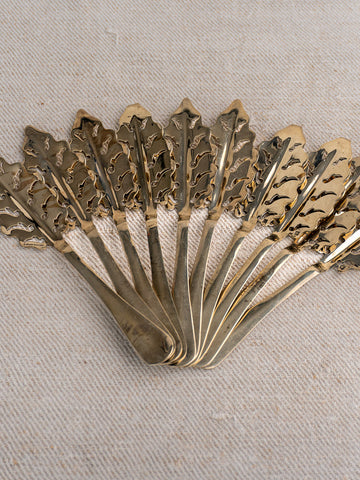 Set of ten antique French absinthe spoons by Cailar Bayard with leaf pattern, displayed on light textured fabric.