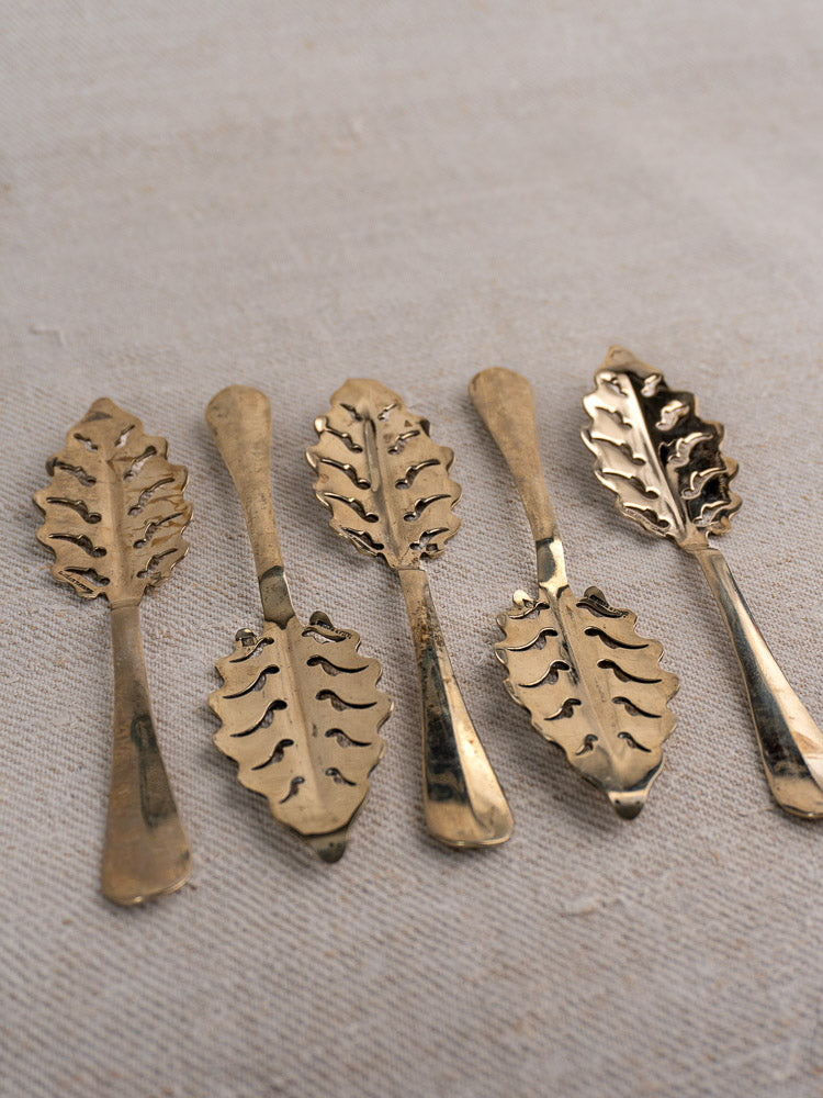 Set of ten Antique French absinthe spoons by Cailar Bayard with leaf handles on light beige fabric.