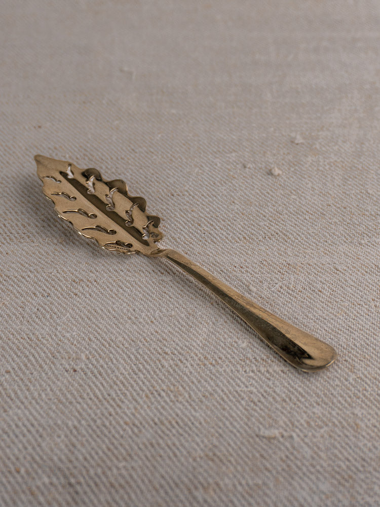 Set of 10 antique French absinthe spoons by Cailar Bayard with gold-toned leaf handles on beige textured fabric.