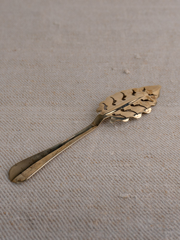 Set of 10 antique French absinthe spoons by Cailar Bayard with gold-toned leaf bowls on beige textured fabric.