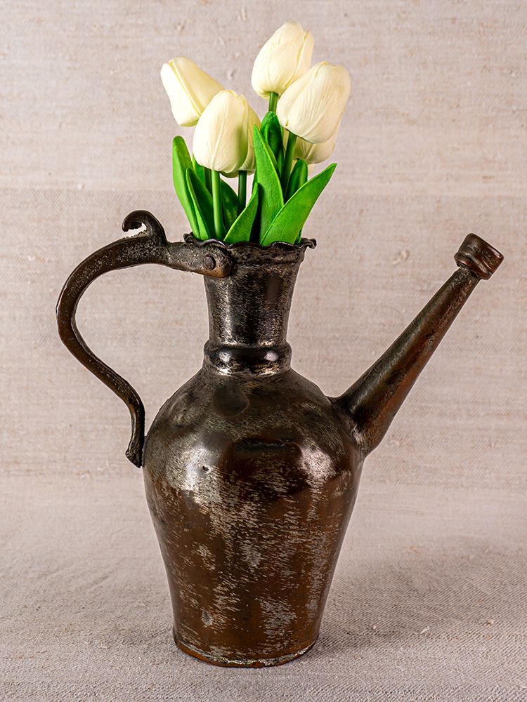 Antique Anatolian tinned copper ibrik repurposed as vase with white tulips, on neutral fabric background.