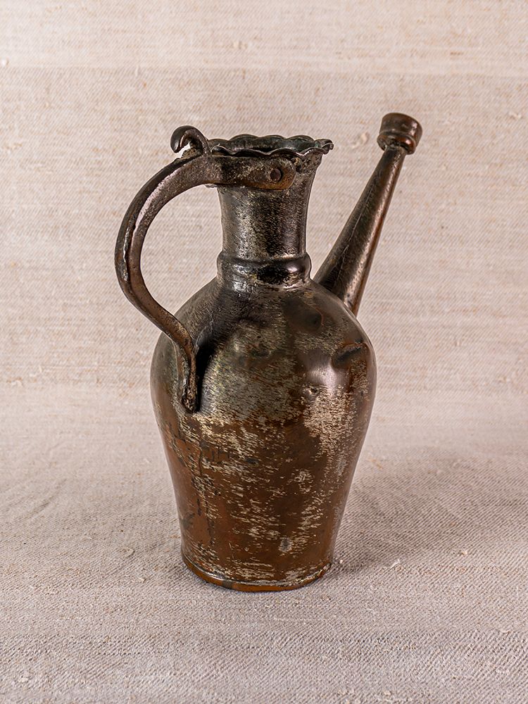 Antique Anatolian tinned copper ibrik with curved handle and long spout on textured beige surface and matching fabric.