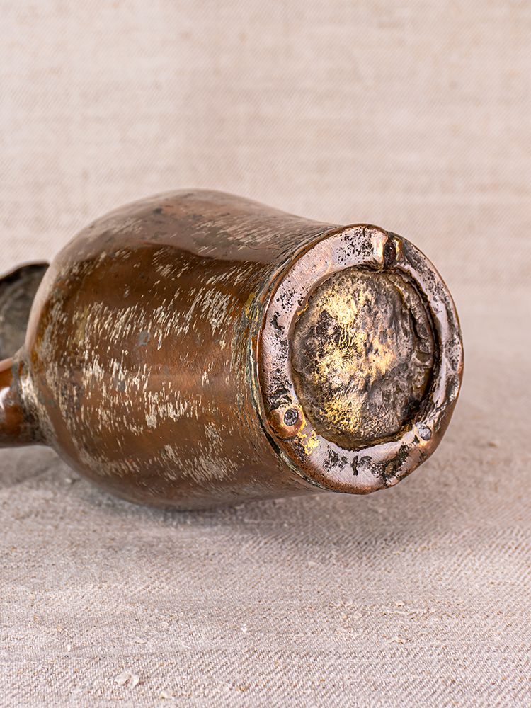 Weathered glass bottle base with faded brown tones and age marks resting on neutral beige fabric.