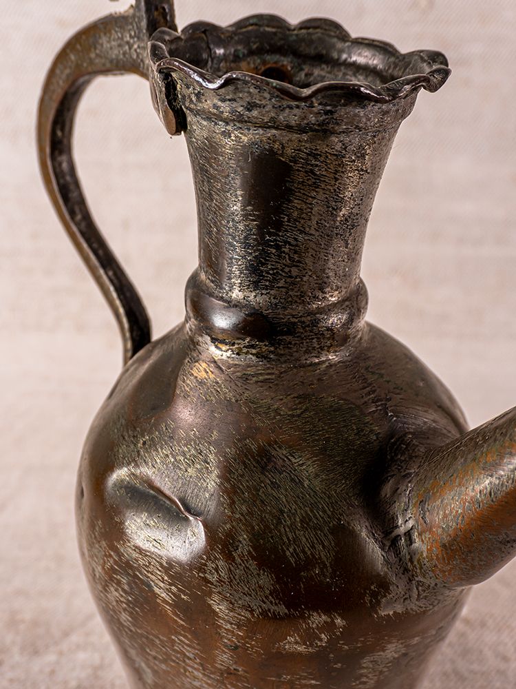 Antique 19th-century Anatolian tinned copper ibrik with scalloped rim and curved handle on a neutral textured background.
