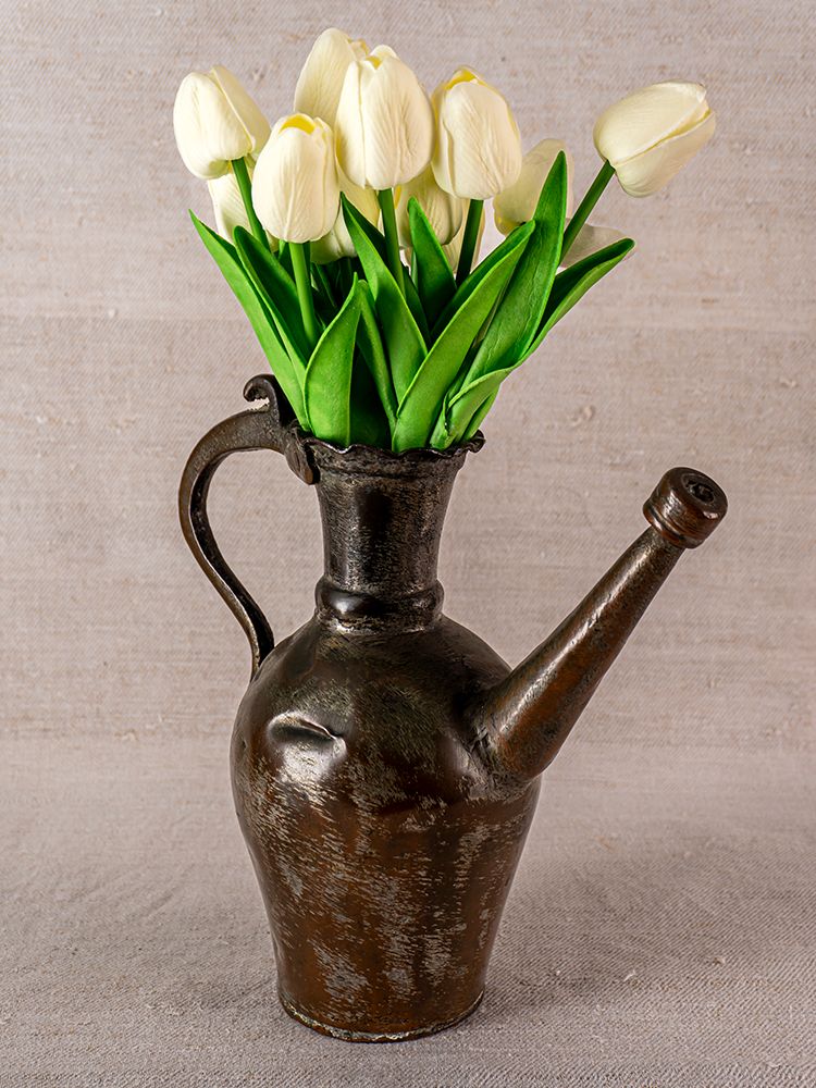19th-century Anatolian tinned copper ibrik used as a vase, with white tulips, on textured beige fabric background.