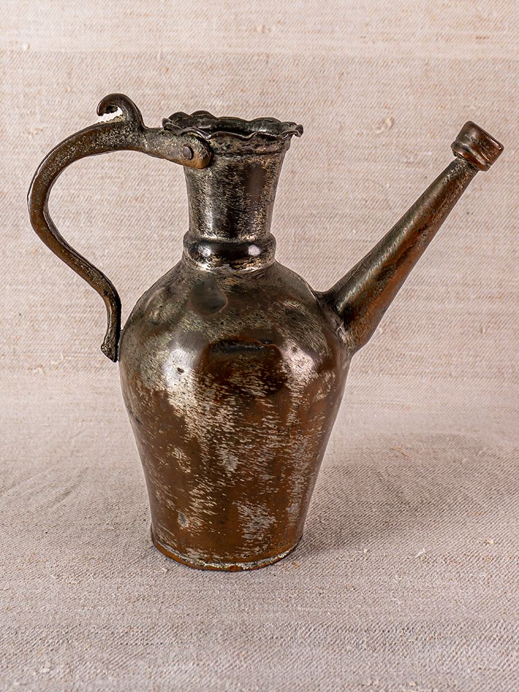 19th-century Anatolian tinned copper ibrik with curved handle and wavy rim, displayed on textured beige fabric.