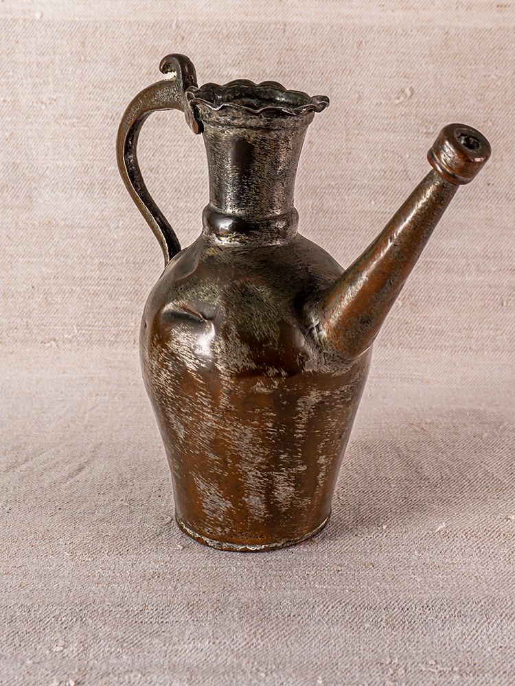 19th-century Anatolian tinned copper ibrik with ornate handle and long spout on a textured beige surface.