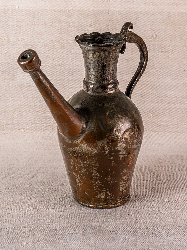 19th-century antique Anatolian tinned copper ibrik with long spout and ornate rim, on textured beige background.