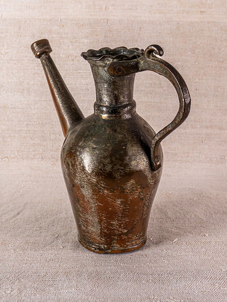 Antique Anatolian tinned copper ibrik watering can with long spout and ornate handle on beige textured surface.