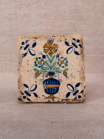 Square hand-painted French faience tile with blue vase, polychrome flowers, and floral motifs on beige.