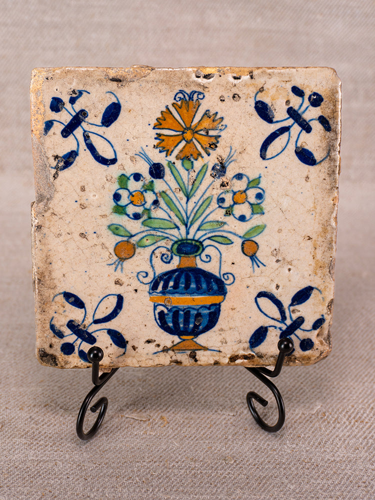 Antique French faience tile with hand-painted blue vase, yellow and green flowers, blue ribbon border on black metal stand.