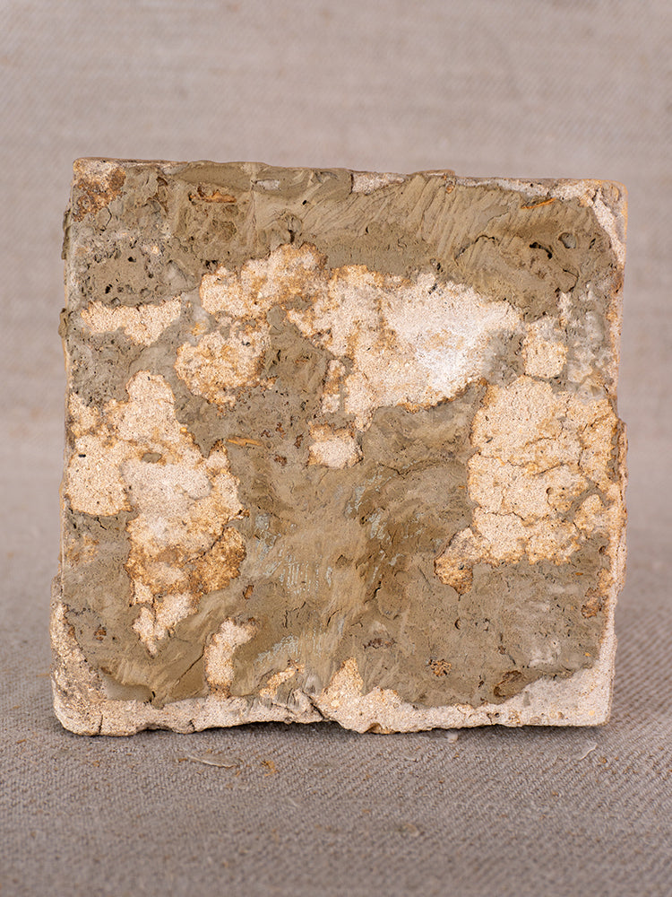 Antique French faience tile with 17th-century polychrome flower vase motif, weathered, on neutral fabric background.