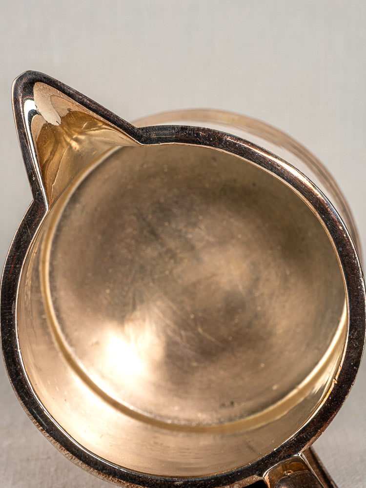 Antique English silver plate milk jug by Walker & Hall, Sheffield, angular rim, on a light surface.