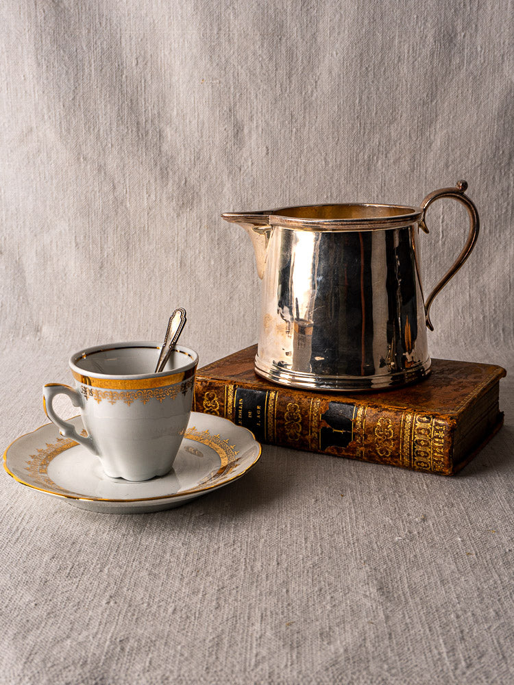 Antique English silver plate milk jug by Walker & Hall, circa 1900, displayed with vintage book and fine teacup set.