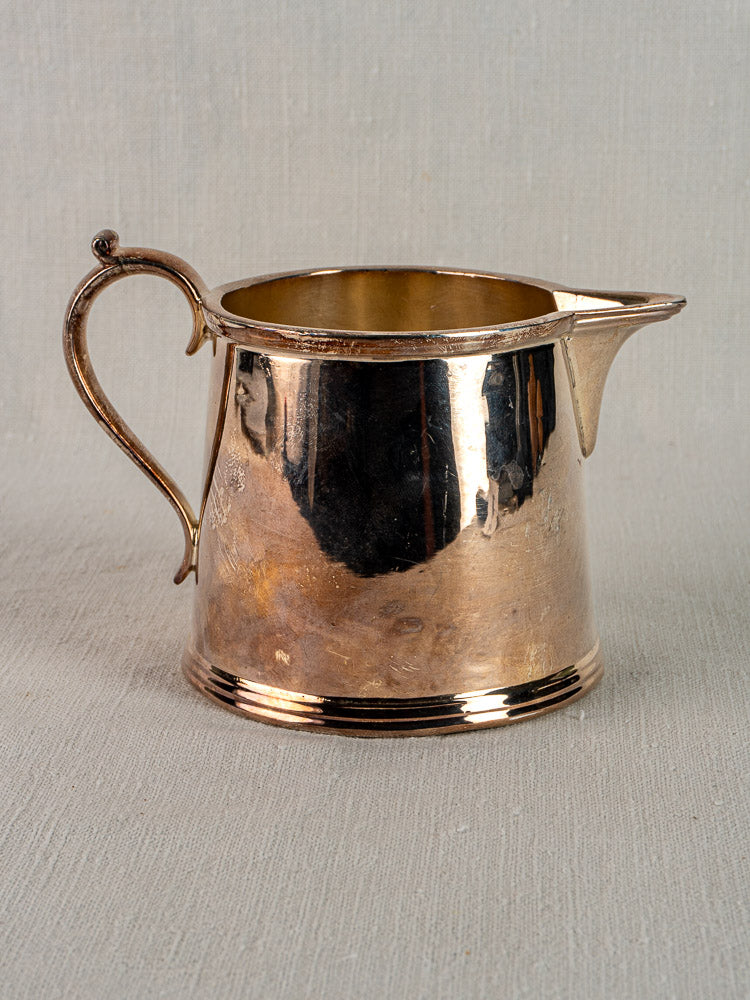 Antique English silver plate milk jug by Walker & Hall, circa 1900, curved handle, decorative base, on neutral fabric background.