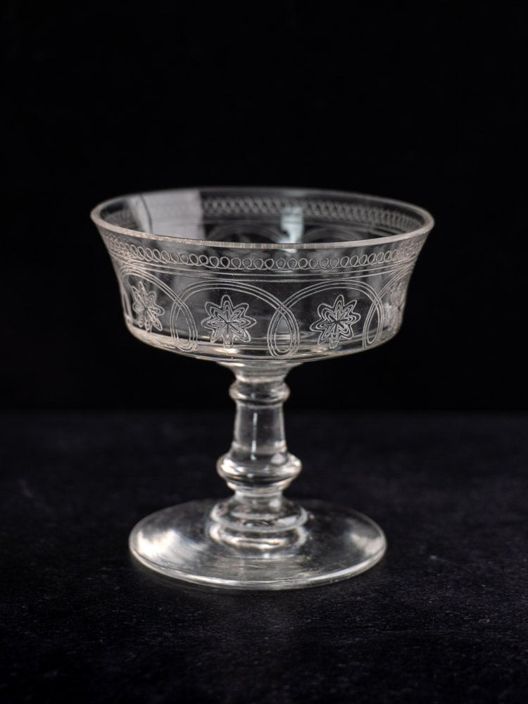 Set of six antique French uranium glass coupes with etched floral and oval motifs, on black background.