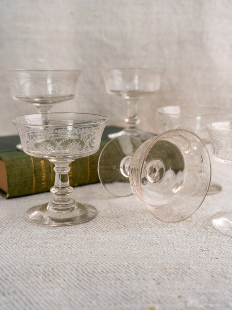 Set of six antique French uranium glass coupes, c. 1900, on textured fabric surface with book.