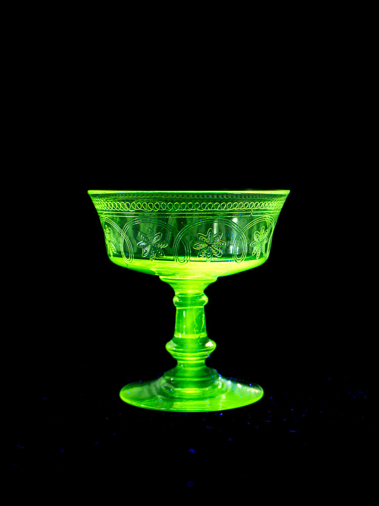 Set of six antique French uranium glass coupes from circa 1900, glowing green against black background.