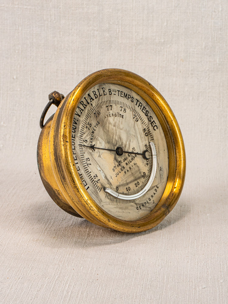 Antique French barometer by Jules Richard Paris, early 20th century brass case, French dial, patina; angled on light fabric.
