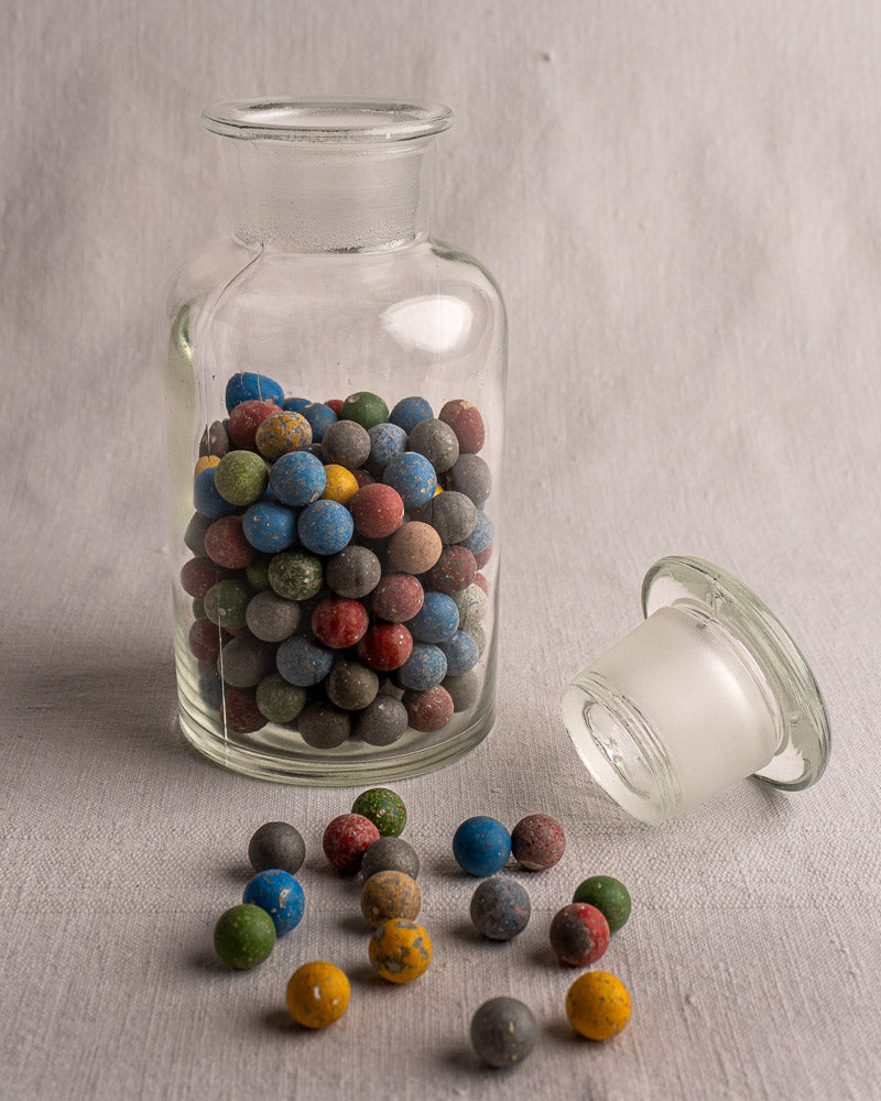 Antique French apothecary jar from c. 1900 with small marbles, on a light gray surface and background.