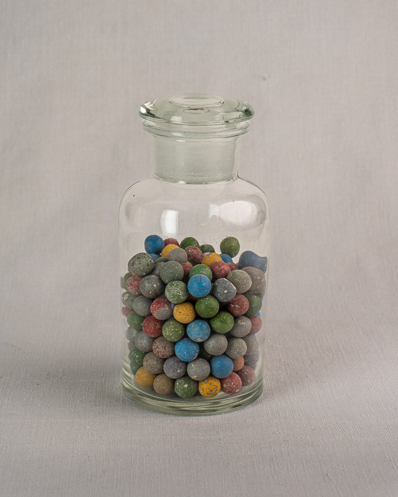Antique French apothecary jar from c. 1900 with small marbles, on a light gray surface and background.