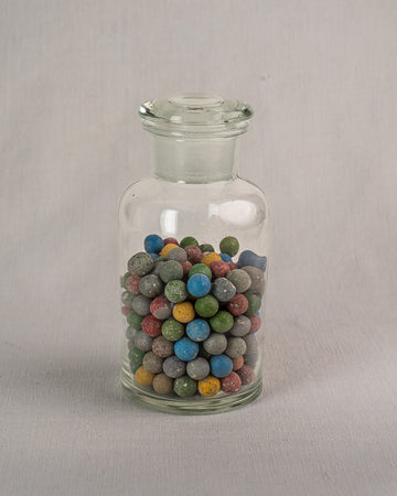 Antique French apothecary jar from c. 1900 with small marbles, on a light gray surface and background.