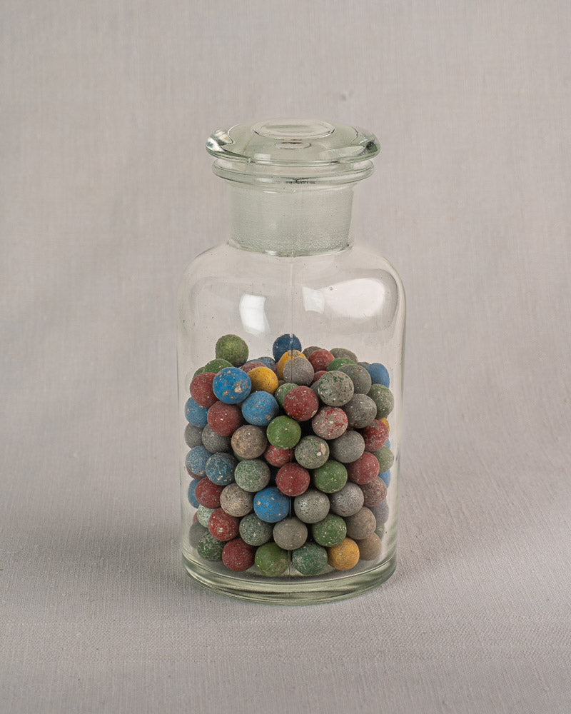 Antique French apothecary jar from the Clay Marble Collection, filled with colorful marbles on a light gray surface.